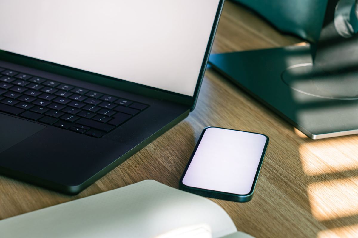 Arbeitsplatz mit aufgeklapptem Notebook, Bildschirm und Smartphone auf einem Holztisch