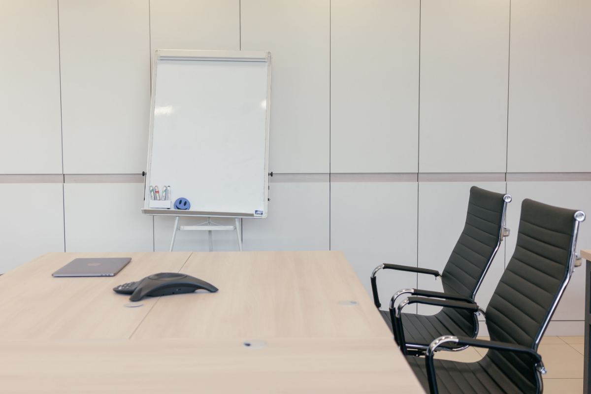 Konferenztelefon auf einem Besprechungstisch, daneben ein zugeklapptes Notebook